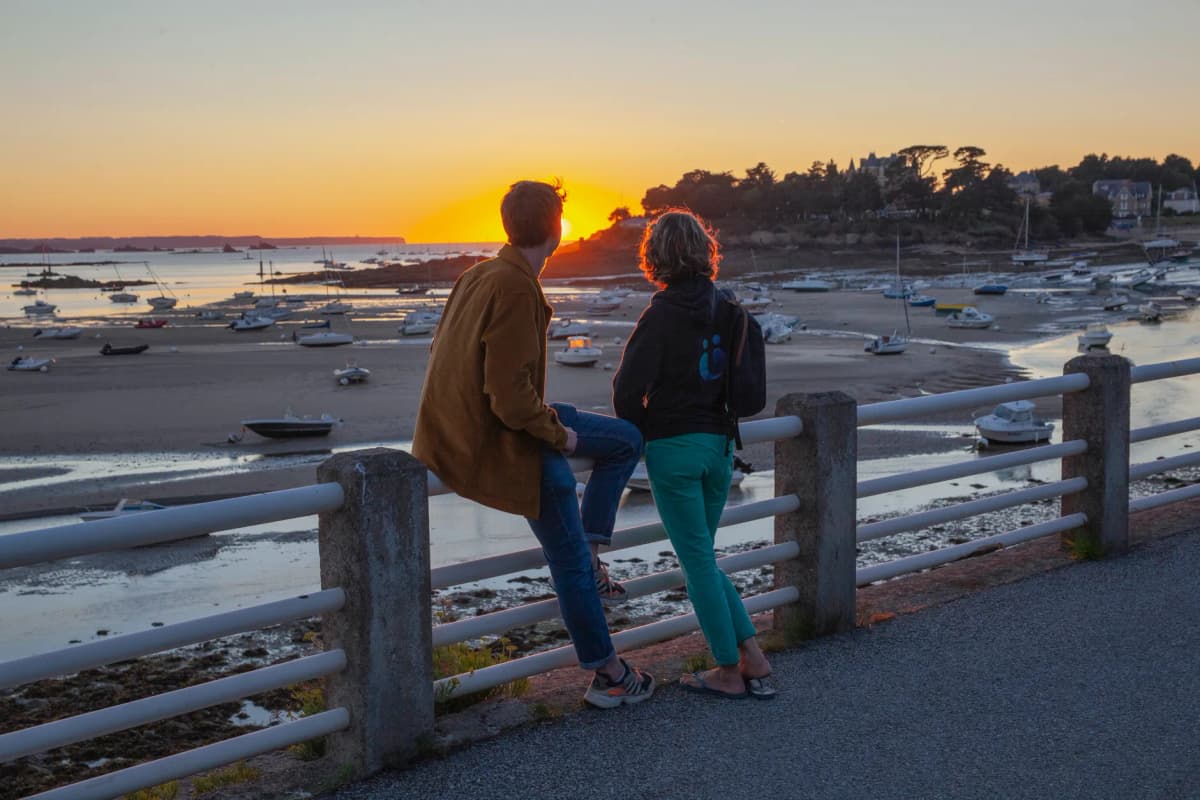 Couple overlooks sunset on the coast of Saint Briac-sur-Mer with boats and low tide landscape.