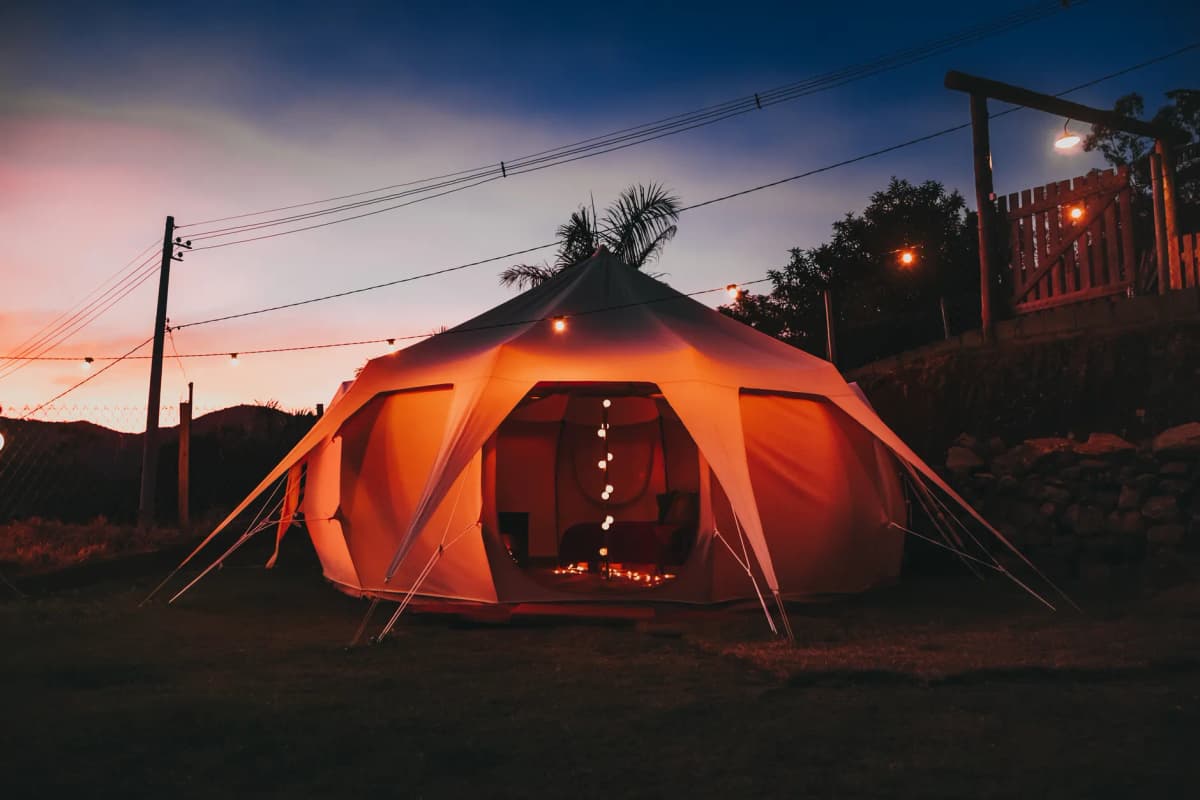 Experience a serene outdoor camping setup with a glowing tent illuminated by string lights against a twilight sky.