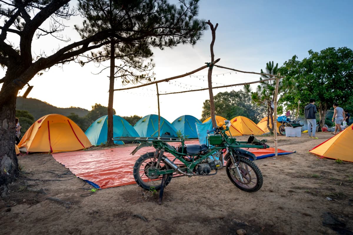 Retro motorcycle parked near camping tents and unrecognizable hikers in mountainous countryside during trip