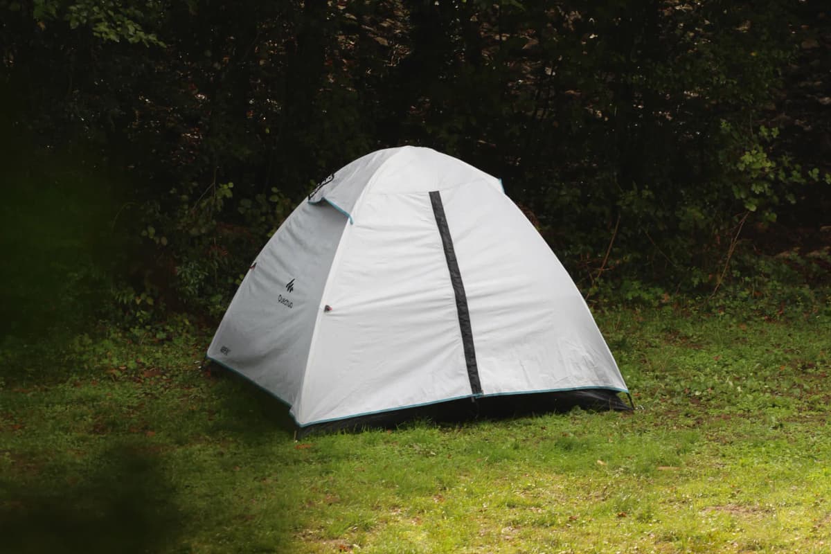 A single white camping tent set in a lush, green forested area, perfect for outdoor retreats.